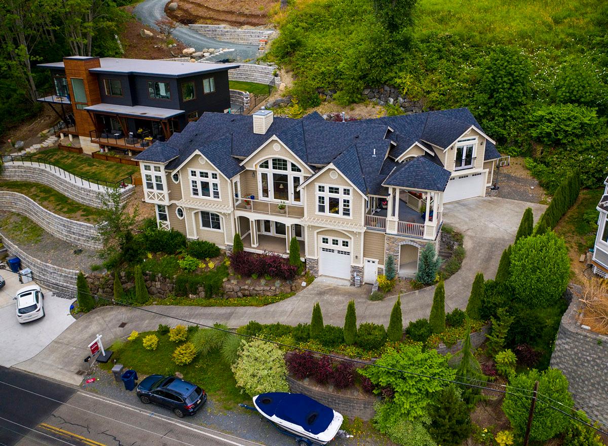 House plan exterior: Beige, multi-story residence with gables, dormers, covered balconies, and a three-car garage.