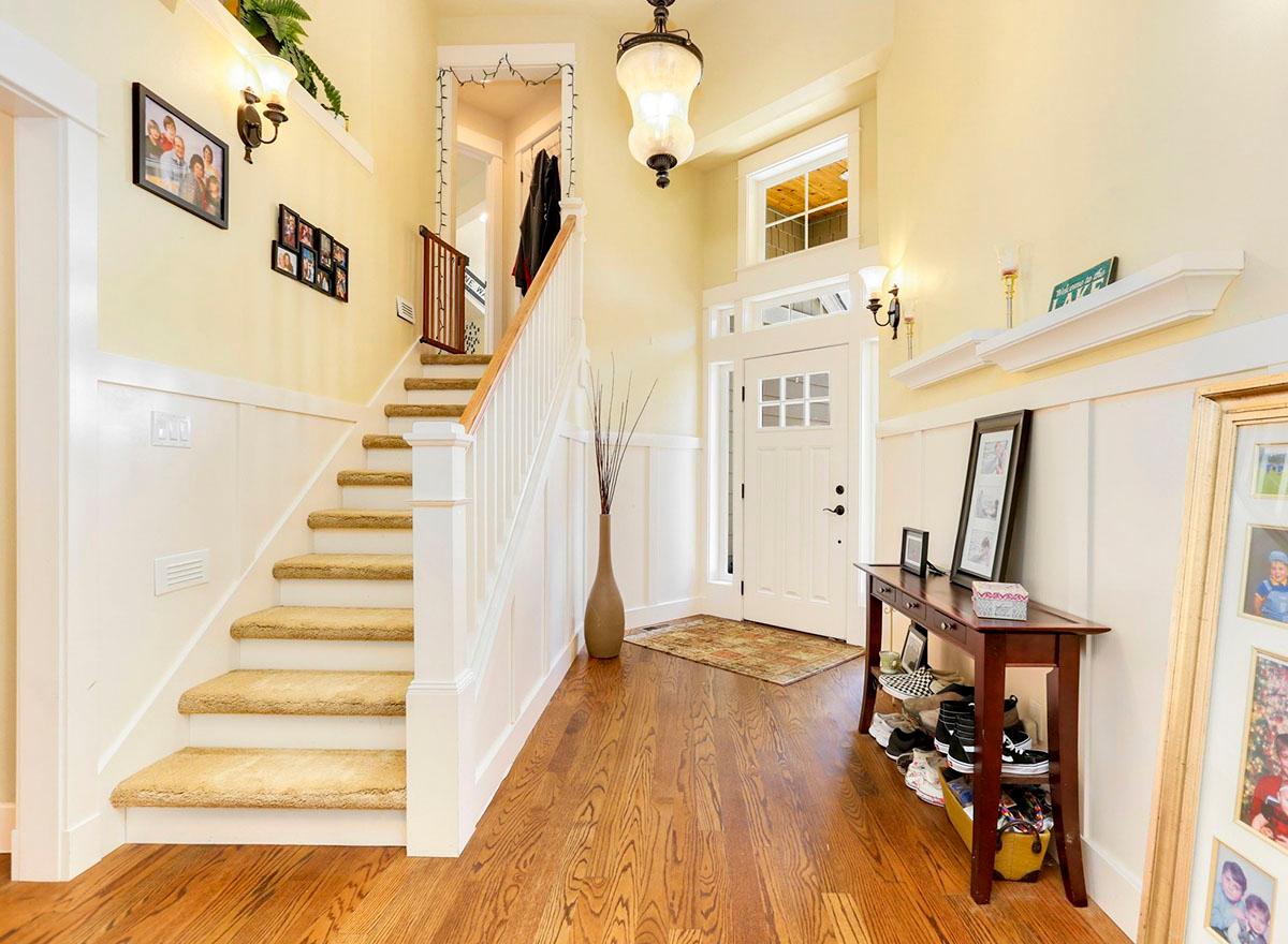 Interior view of a hallway with a staircase, entry door with glass panes, and wood flooring.