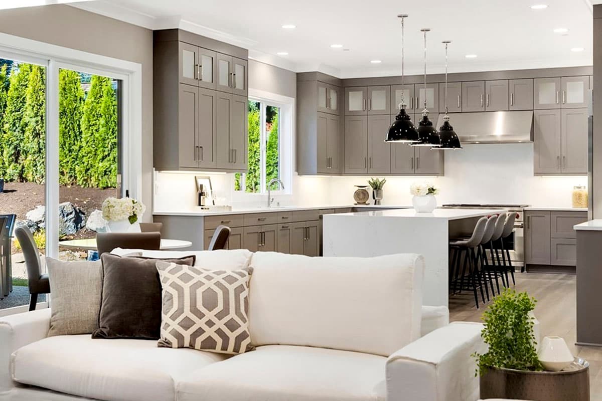 Open concept kitchen with gray cabinets, large island, pendant lights, and adjacent living area with sofa.