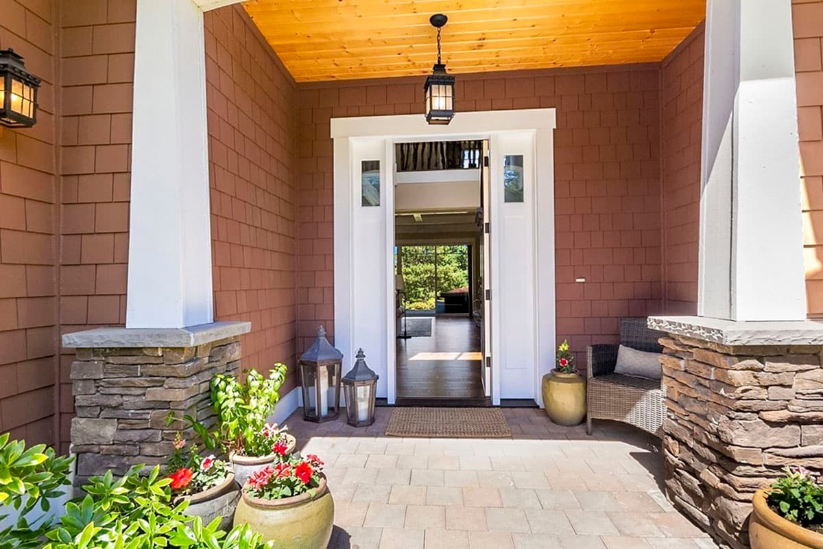 House plan exterior: covered entry with stone pillars, shingle siding, double front doors, and wood plank ceiling.