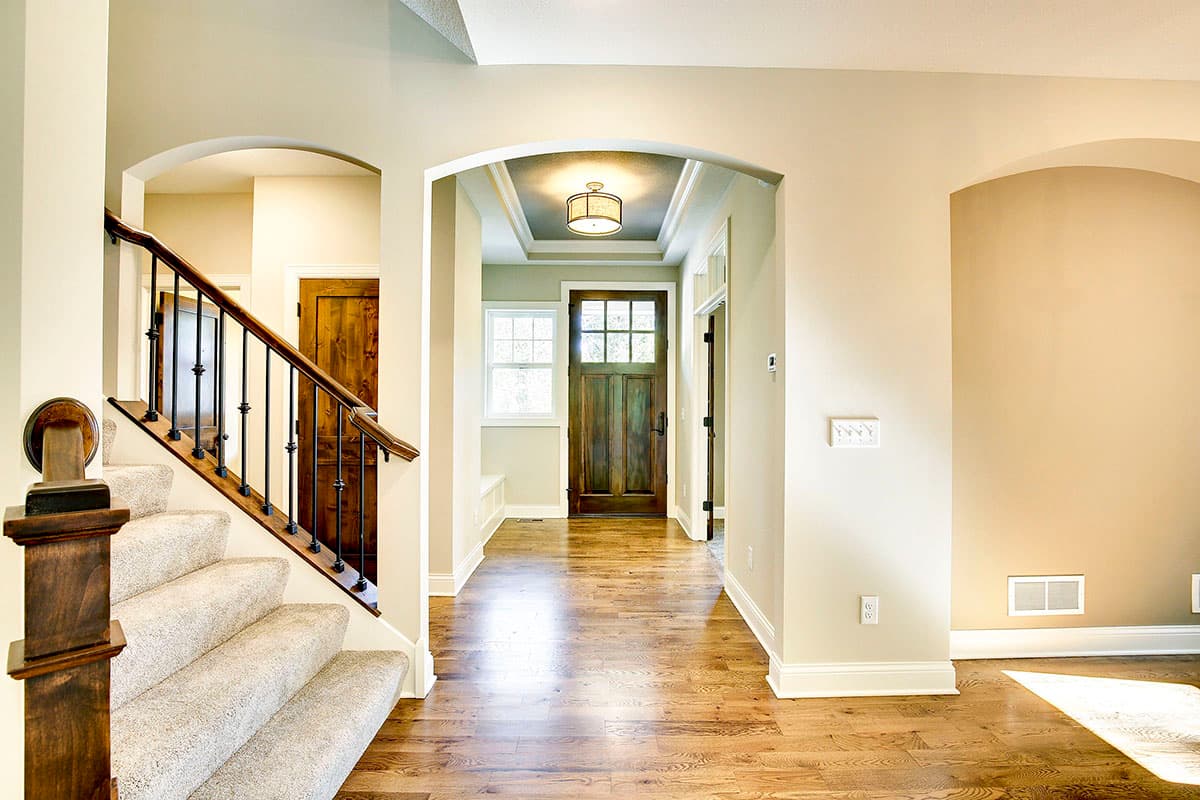 Interior view of an entryway with a carpeted staircase, wooden front door, and hardwood flooring.