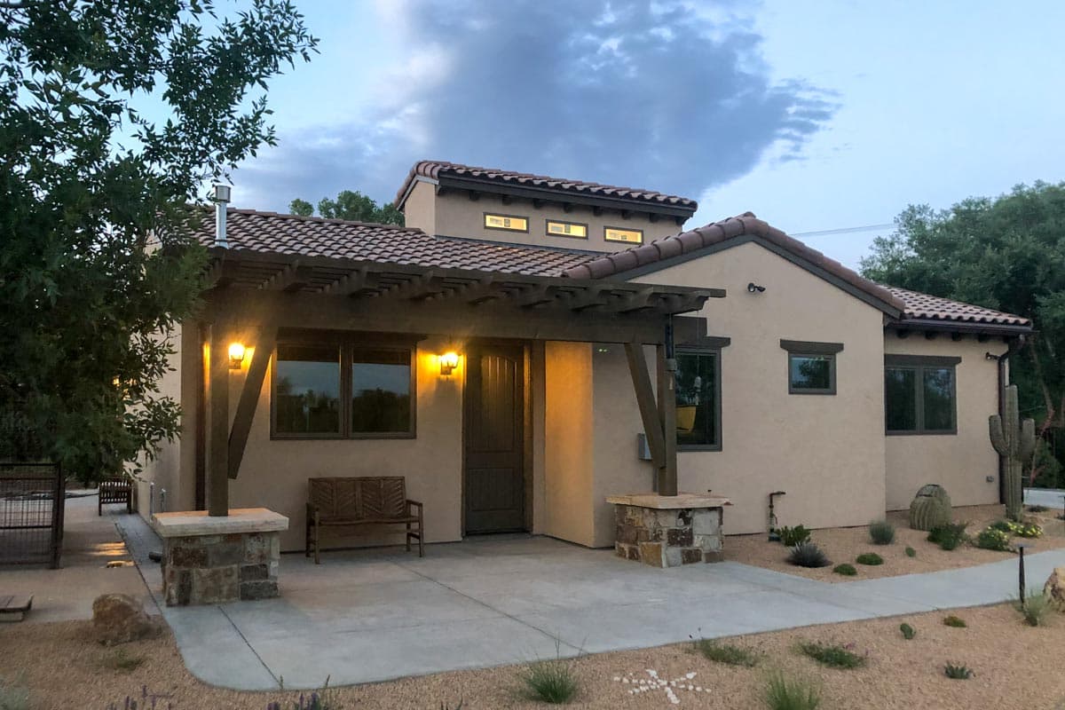 House plan exterior. One-story stucco home with pergola covered entry, Spanish tile roof, and multiple gables.