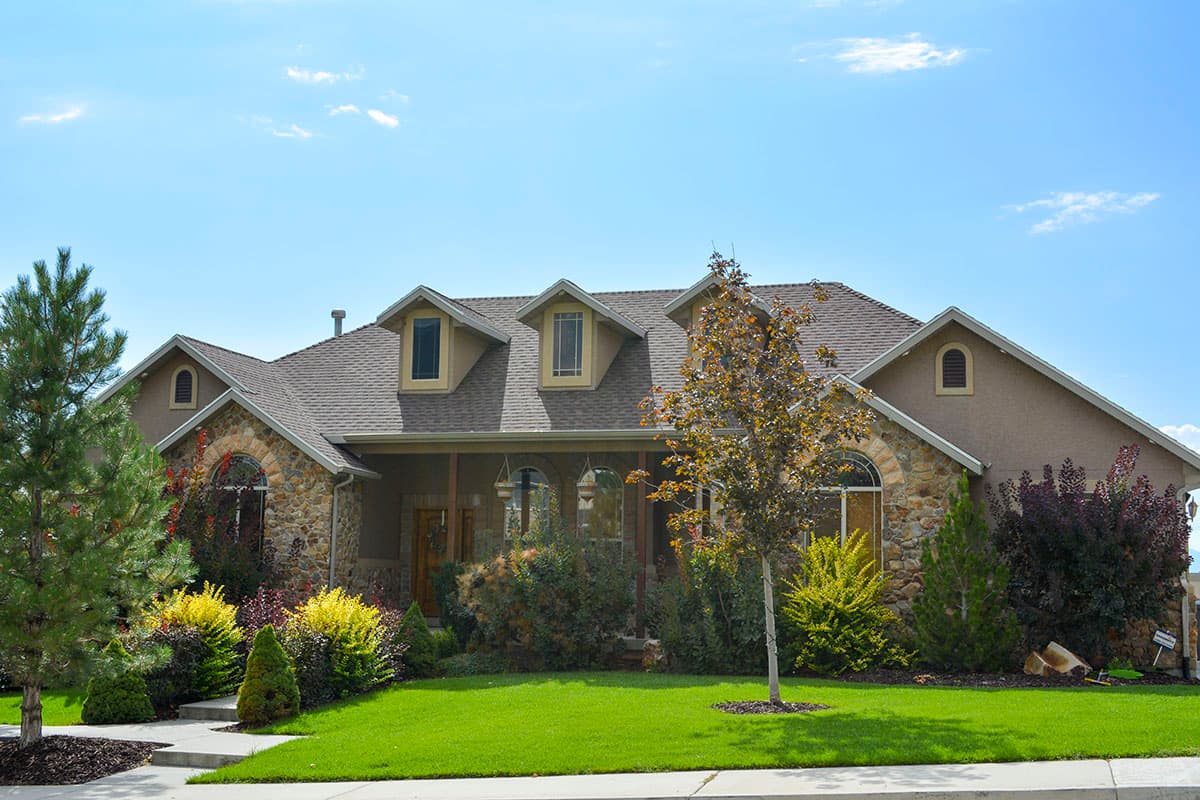 House plan exterior of a sprawling one-story home with stone accents, a covered porch, and three gabled dormers.