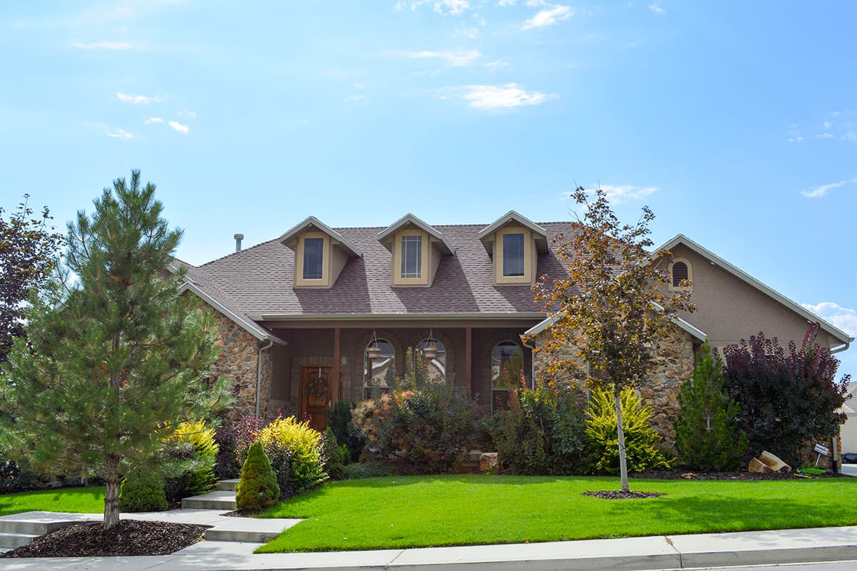 House plan exterior with stone accents, covered porch, arched windows, and multiple dormer windows.