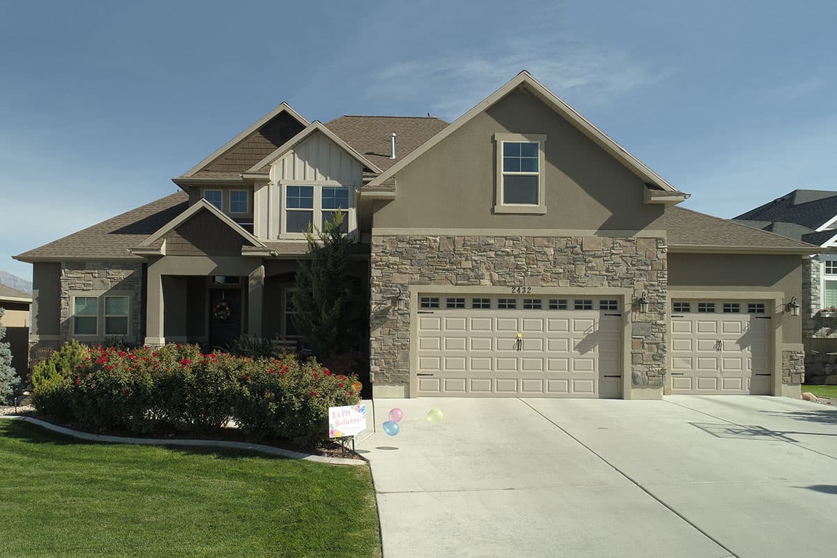 House plan exterior: Two-story home with stone accents, multiple gables, a covered entry, and a three-car garage.