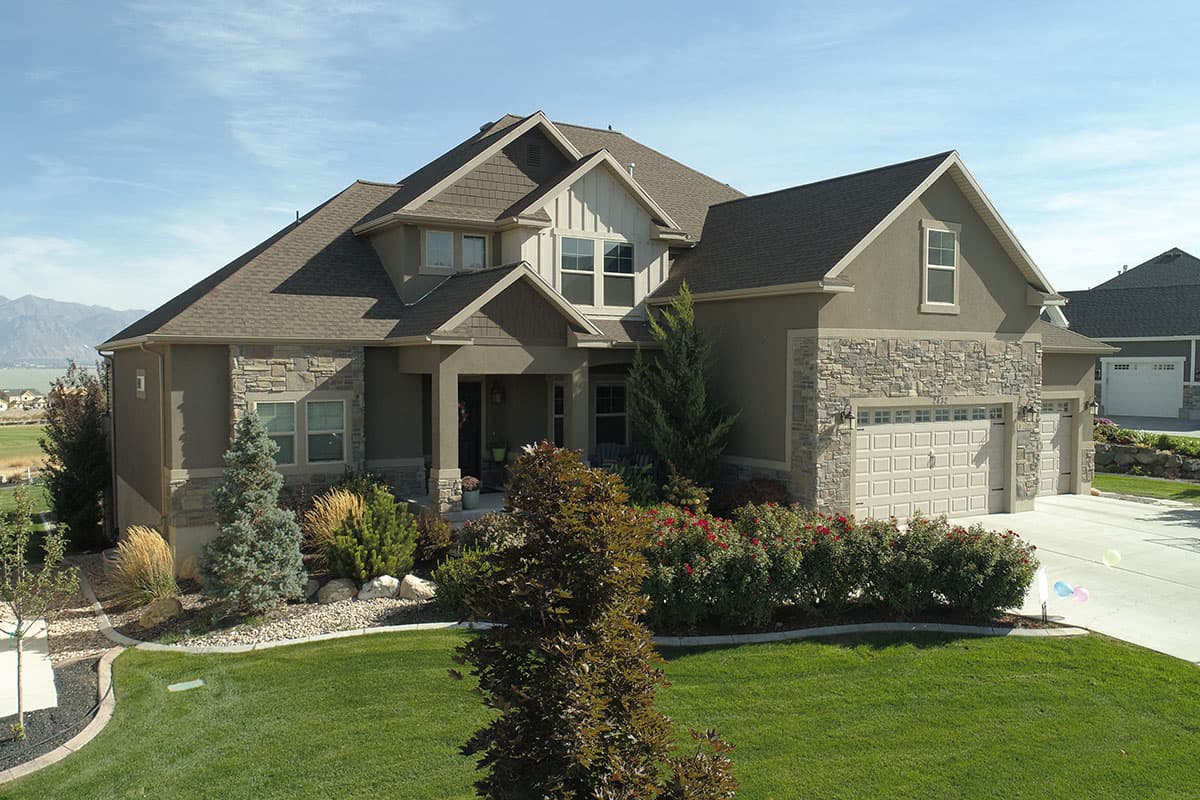 House plan exterior: Two-story Modern Farmhouse with stone accents, prominent gables, covered entry porch, and a three-car garage.