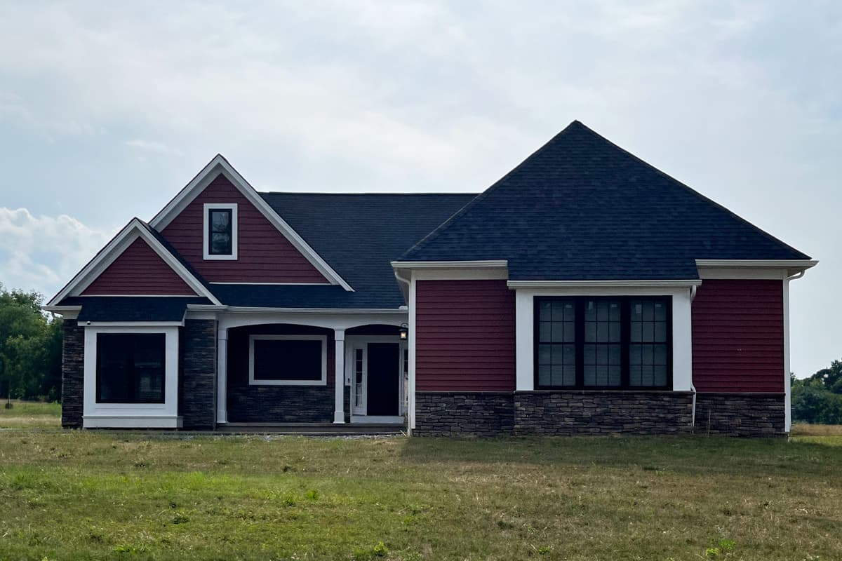 House plan exterior: single-story, dark red siding, stone foundation, prominent gables, and covered entry with columns.