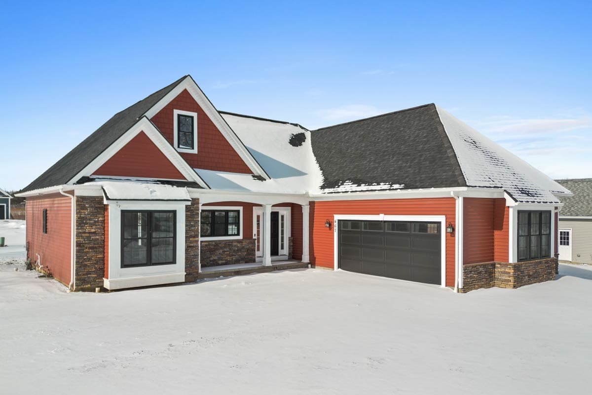 House plan exterior: Red siding, stone accents, gables, dormer, covered entry, attached garage.
