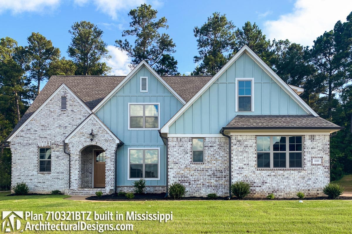 House plan exterior featuring white brick, light blue vertical siding, multiple gables, and an arched entryway.
