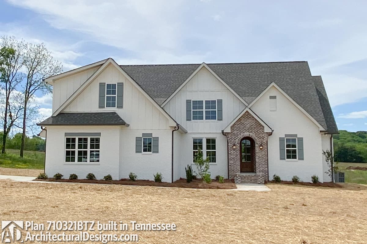 House plan exterior: white brick, white siding, multiple gables, arched brick entry, dormer windows, and hip roof.