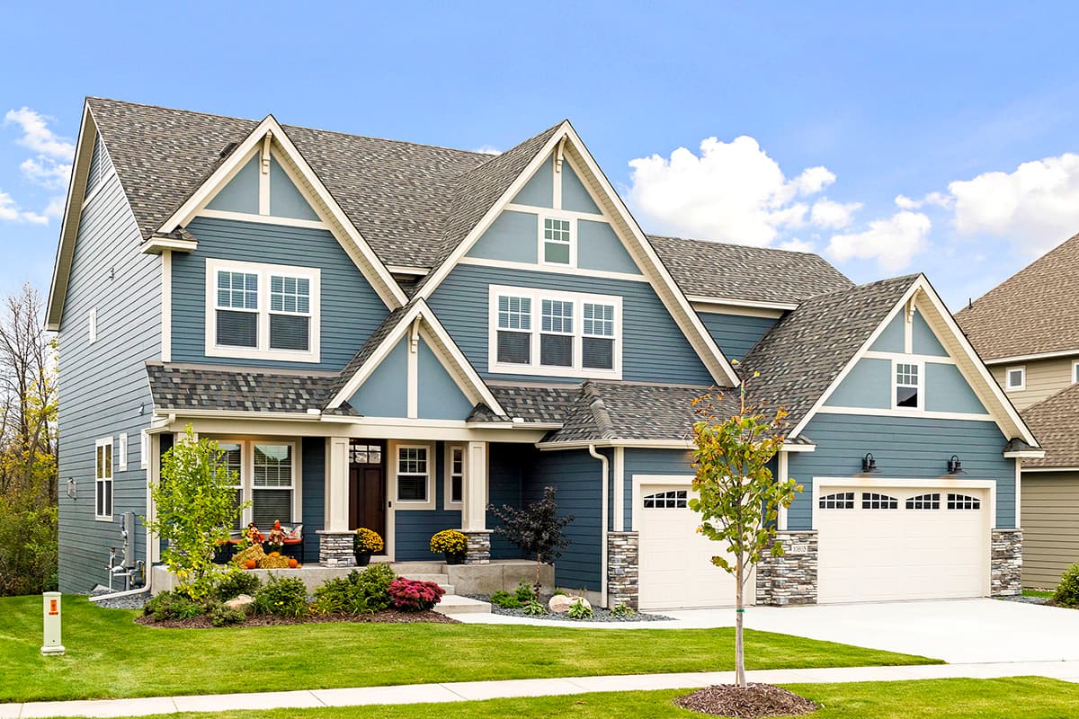 Two-story house plan exterior with gables, dormers, a covered porch, stone accents, and a three-car garage.