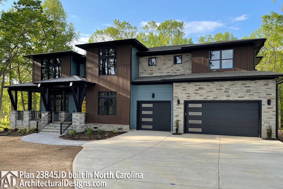 Modern two-story house plan exterior with layered stone, wood siding, blue panels, covered porch, and dark modern garage doors.