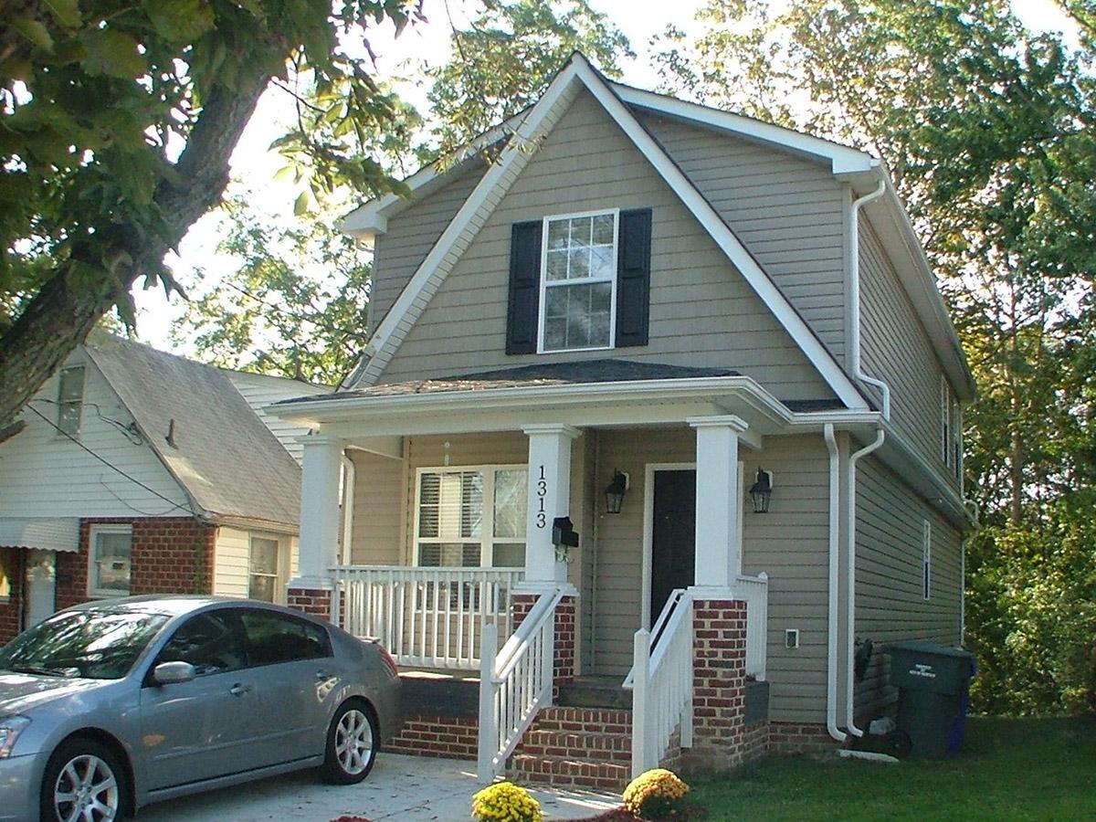 House plan exterior. Two-story Craftsman home with a front porch supported by columns. Features include gabled roof, dormer, and brick accents.