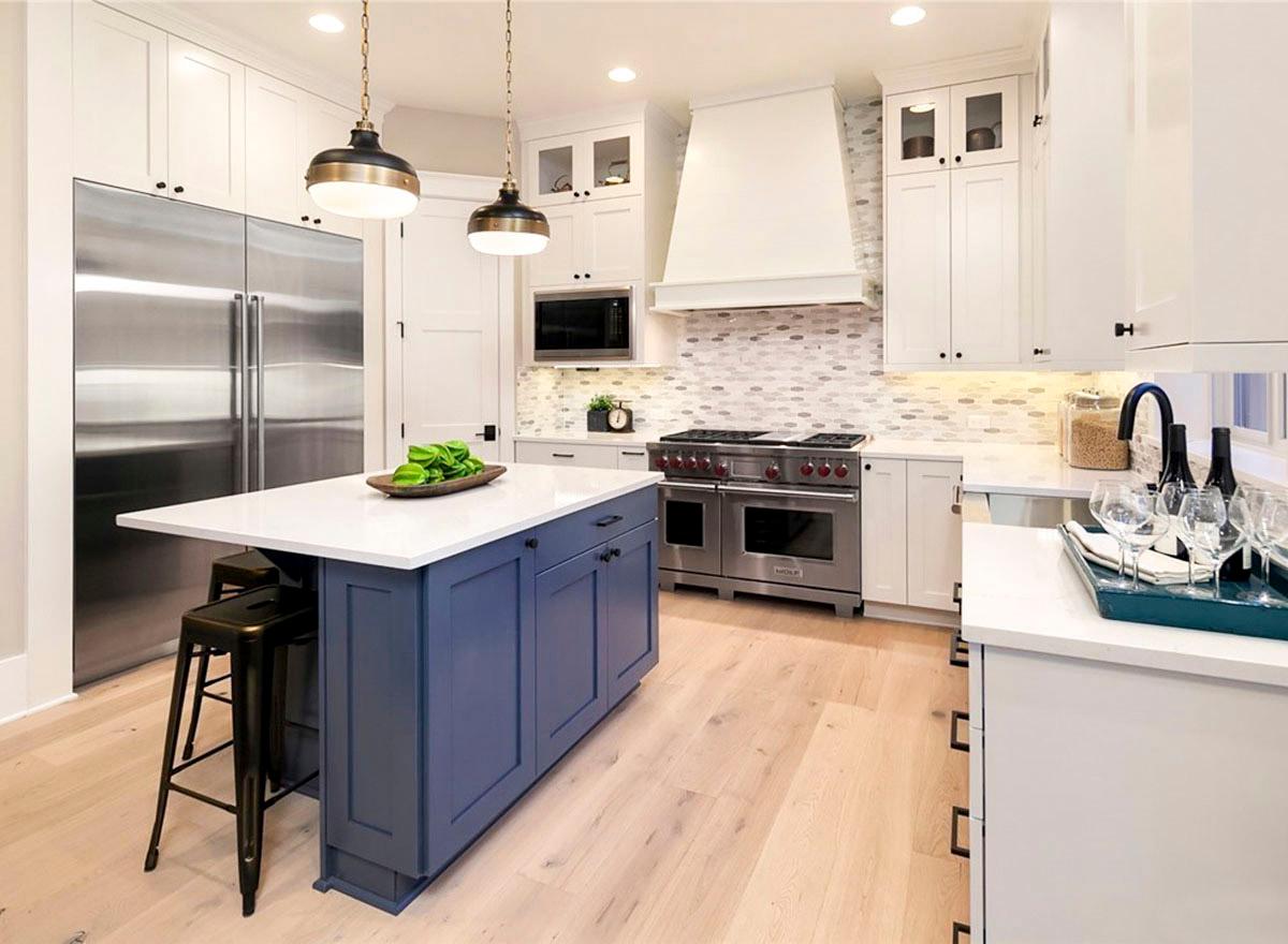 Interior view of a modern kitchen with a central island, professional range, stainless steel refrigerator, white cabinetry, and pendant lighting.
