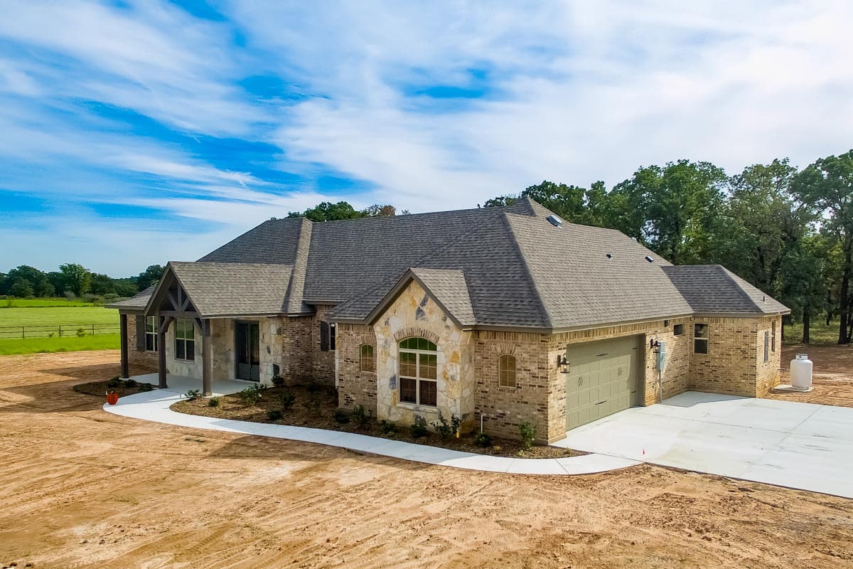 House plan exterior: Ranch style, brick construction, prominent gables, covered front porch with timber accents, attached side-entry garage.