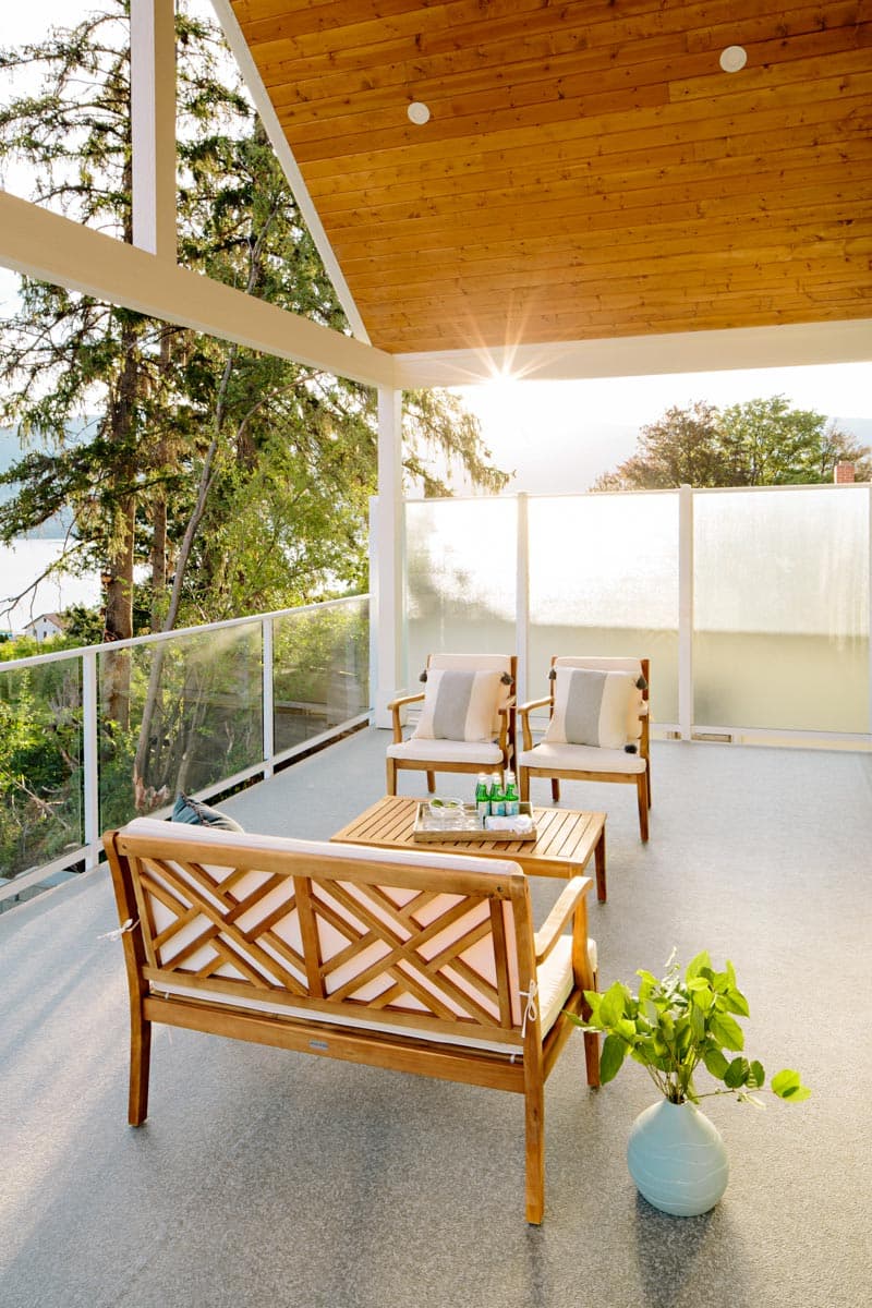 Covered porch with wood ceiling, glass railings, and outdoor seating.