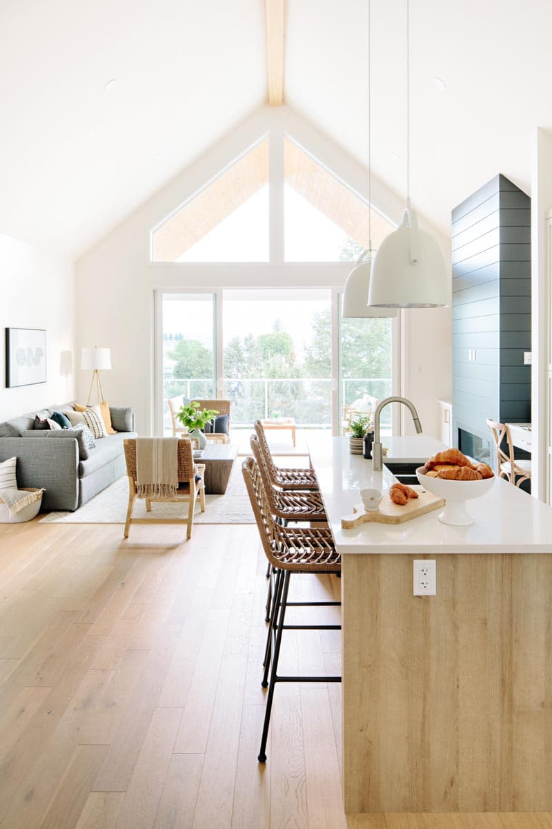 Modern open-concept living area with vaulted ceiling, large windows, island with seating, and gray sofa.