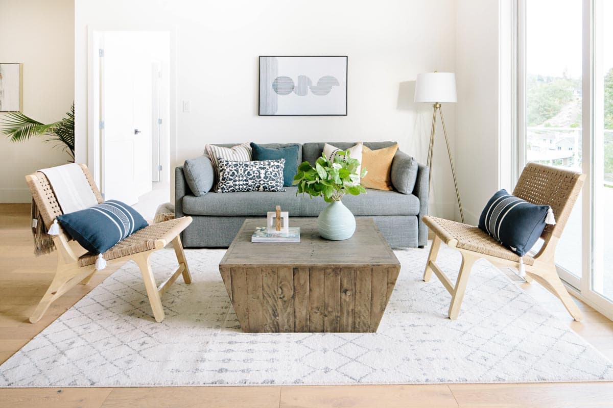 Interior rendering of a living room with a gray sofa, two woven chairs, and a wooden coffee table.