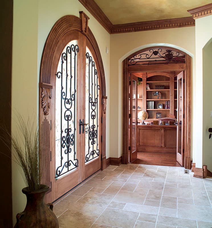 Interior entryway with double arched wooden doors featuring wrought iron, leading to a study with built-in bookshelves.