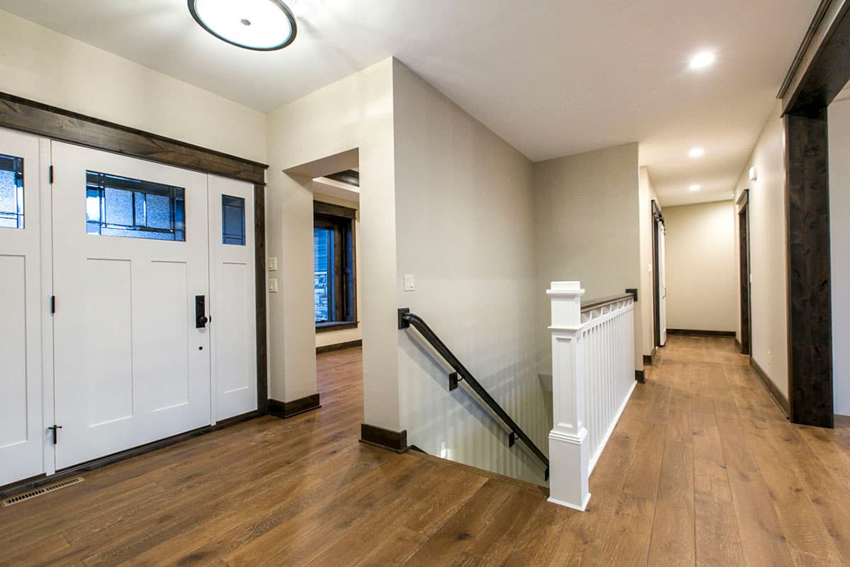 Interior view: Entryway with double doors, wood flooring, staircase with white railing, and hallway leading to rooms.