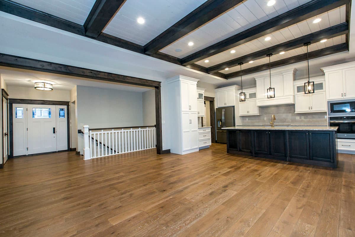 Open concept living area with beamed ceiling, kitchen island, and double front doors leading to a staircase.