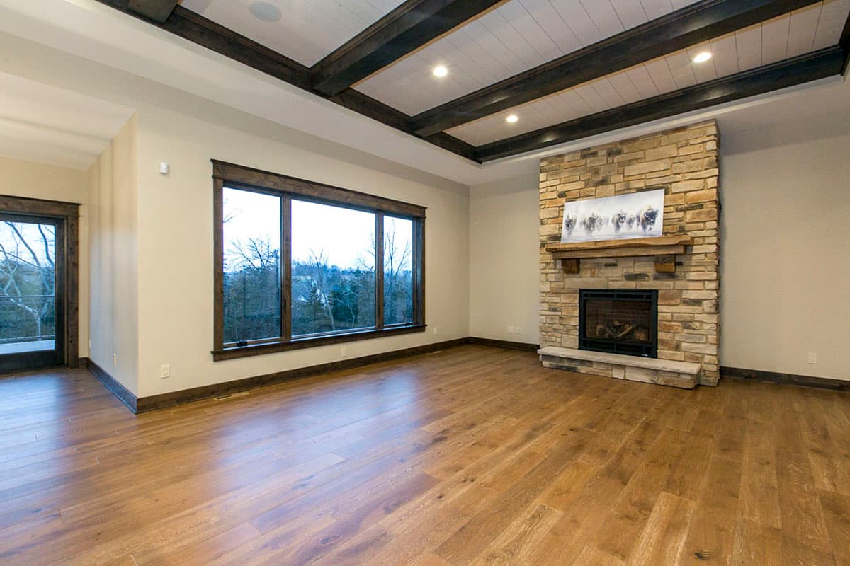 Living room interior with stone fireplace, large picture window, wood-beamed ceiling, and hardwood floors.