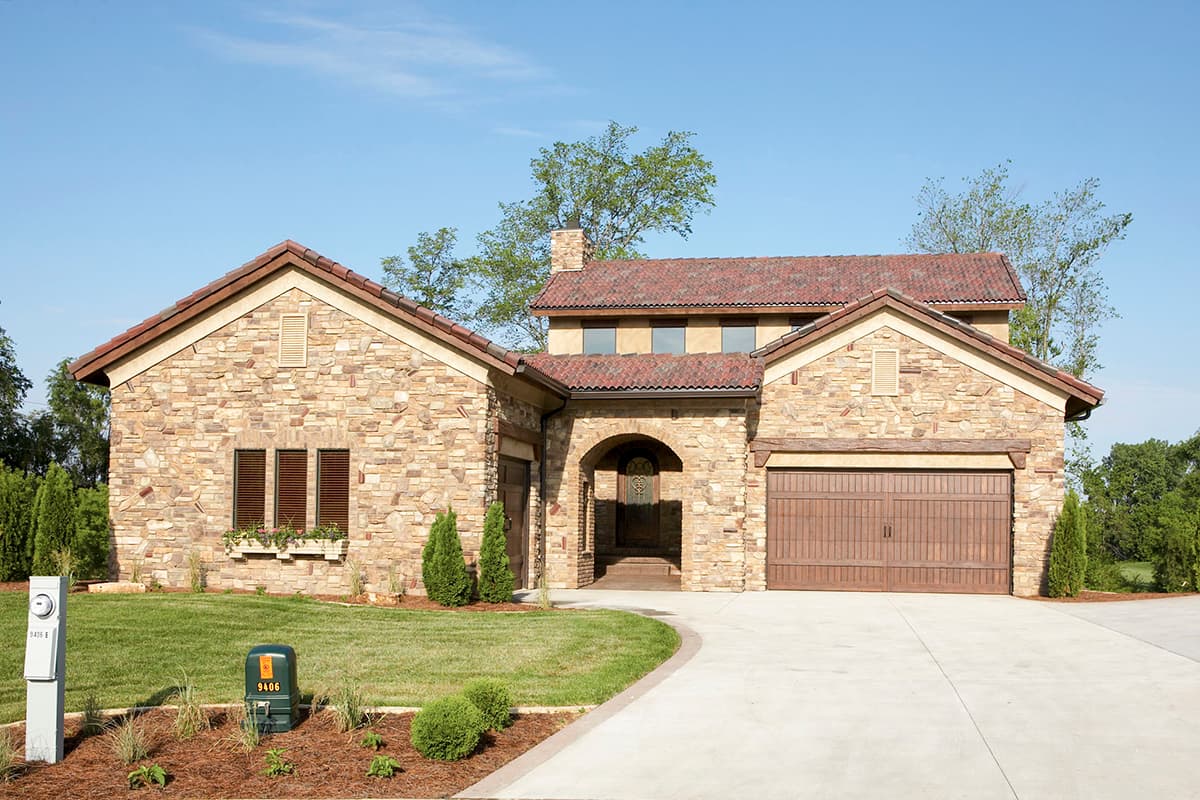 House plan exterior with stone veneer, tile roof, arched entryway, and attached garage. The two-story home also has multiple gables.