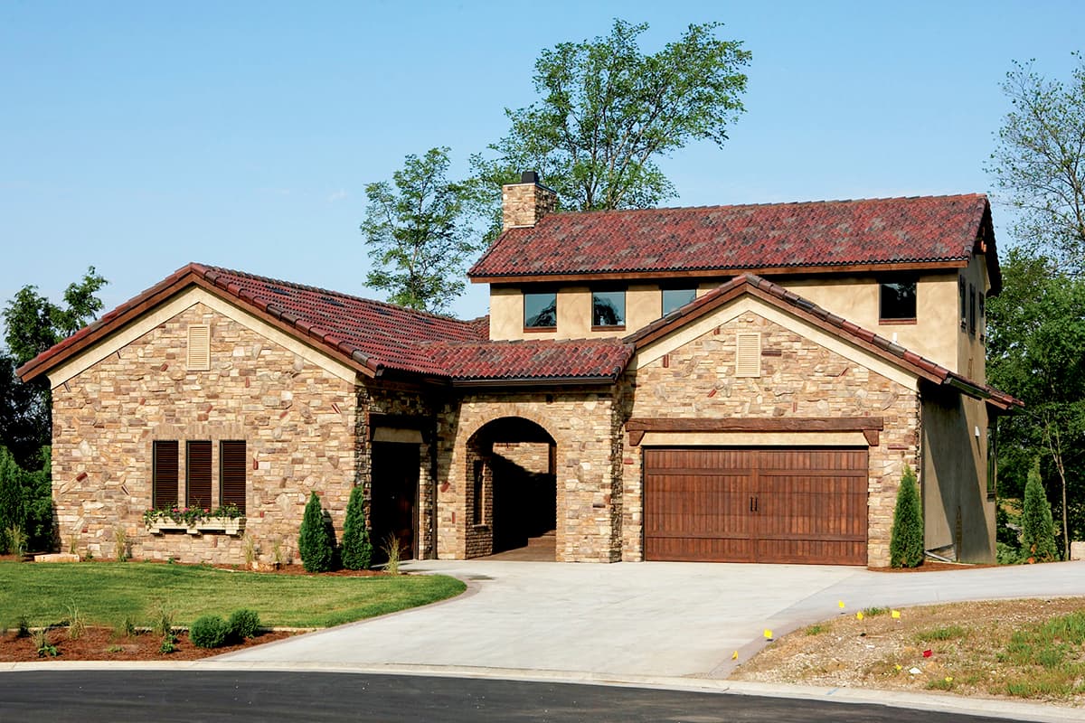 House plan exterior: Tuscan style with stone facade, red tile roof, arched entryway, and double garage door.