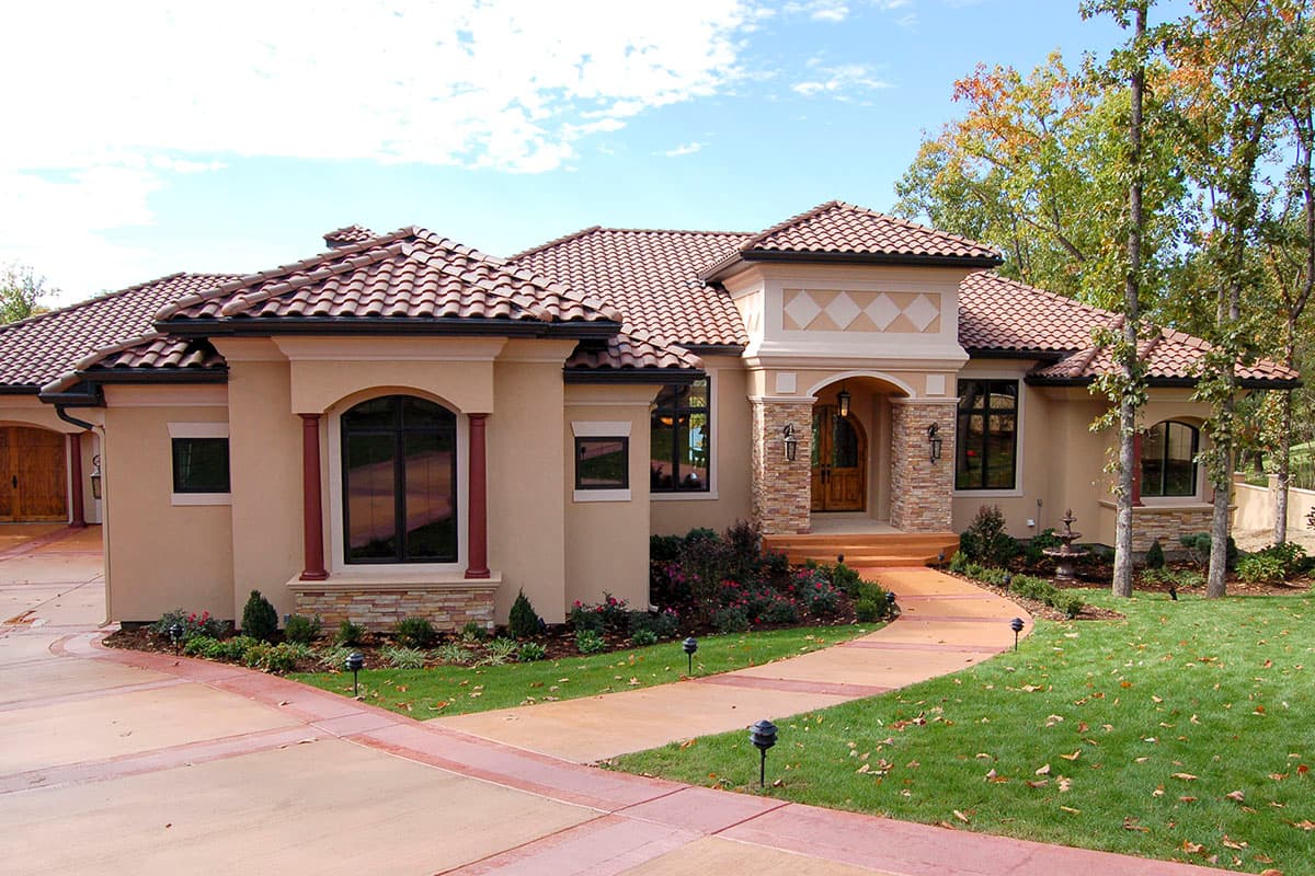 House plan exterior. Mediterranean-style home with tile roof, arched entry, and stucco facade. Features include a curved pathway and multiple windows.