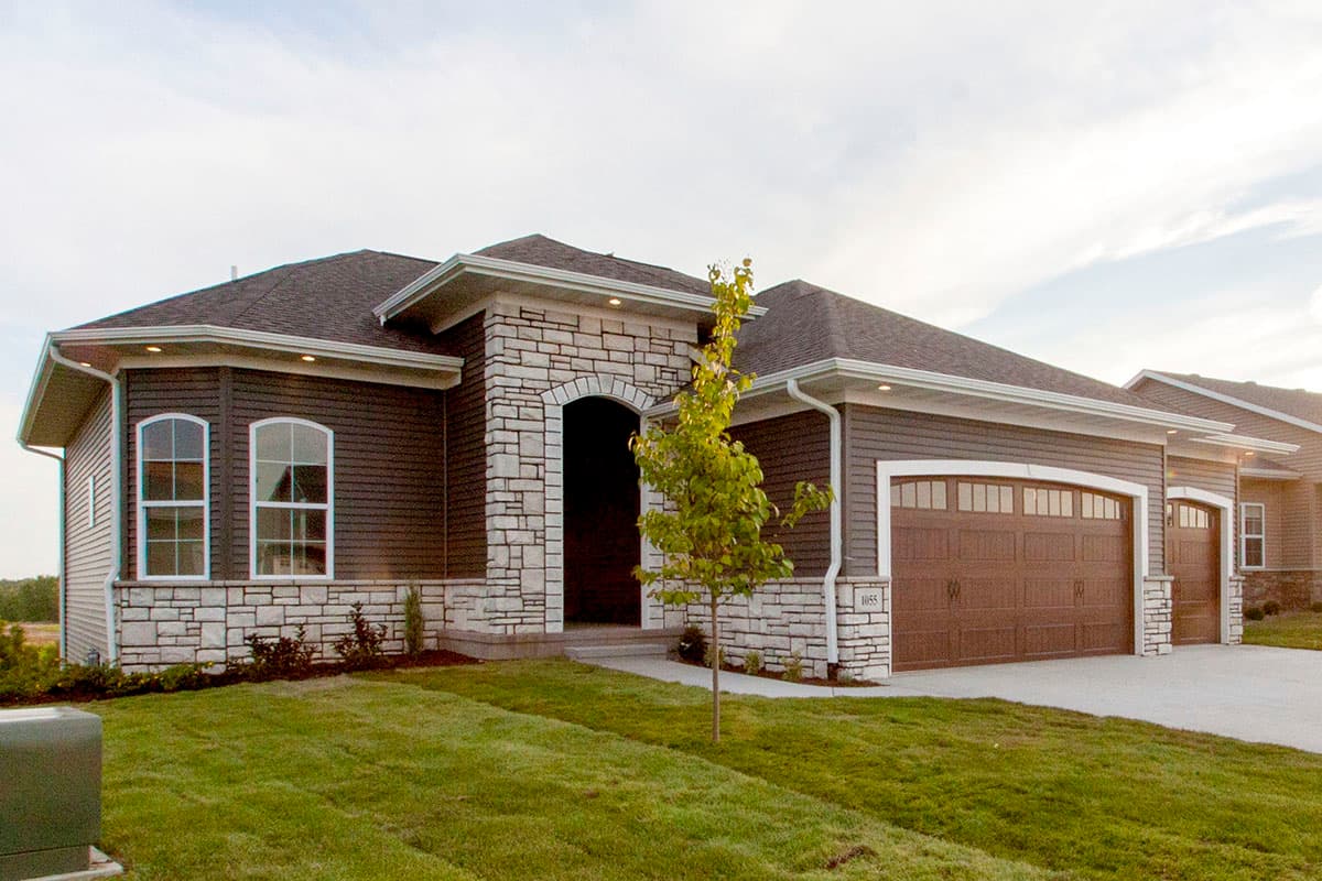 House plan exterior. Ranch style with a stone facade entry and garage, dual gable roof, and attached two-car garage.