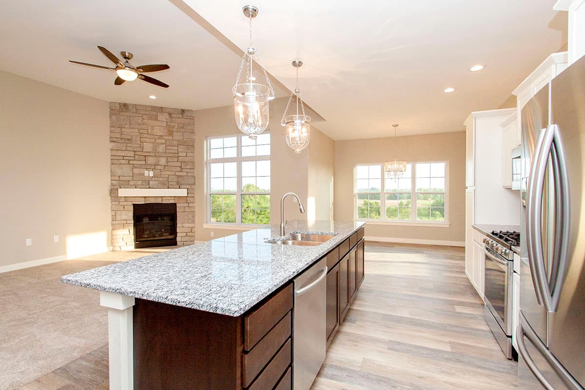 Open concept kitchen and living area with stone fireplace, large island with sink, stainless steel appliances, and abundant natural light.