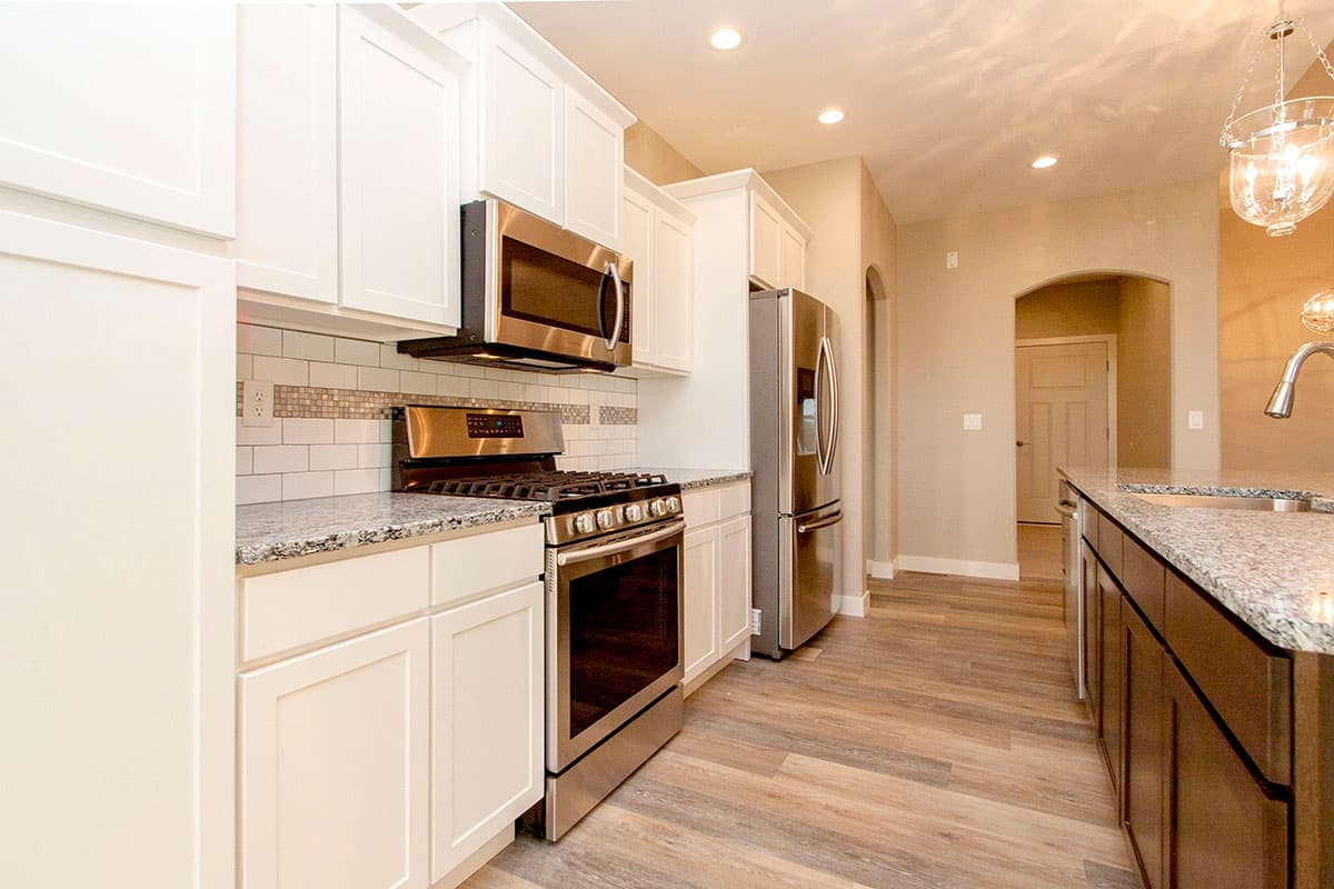 Kitchen interior with stainless steel gas range, microwave, refrigerator, granite countertops, white cabinets, and arched doorway.