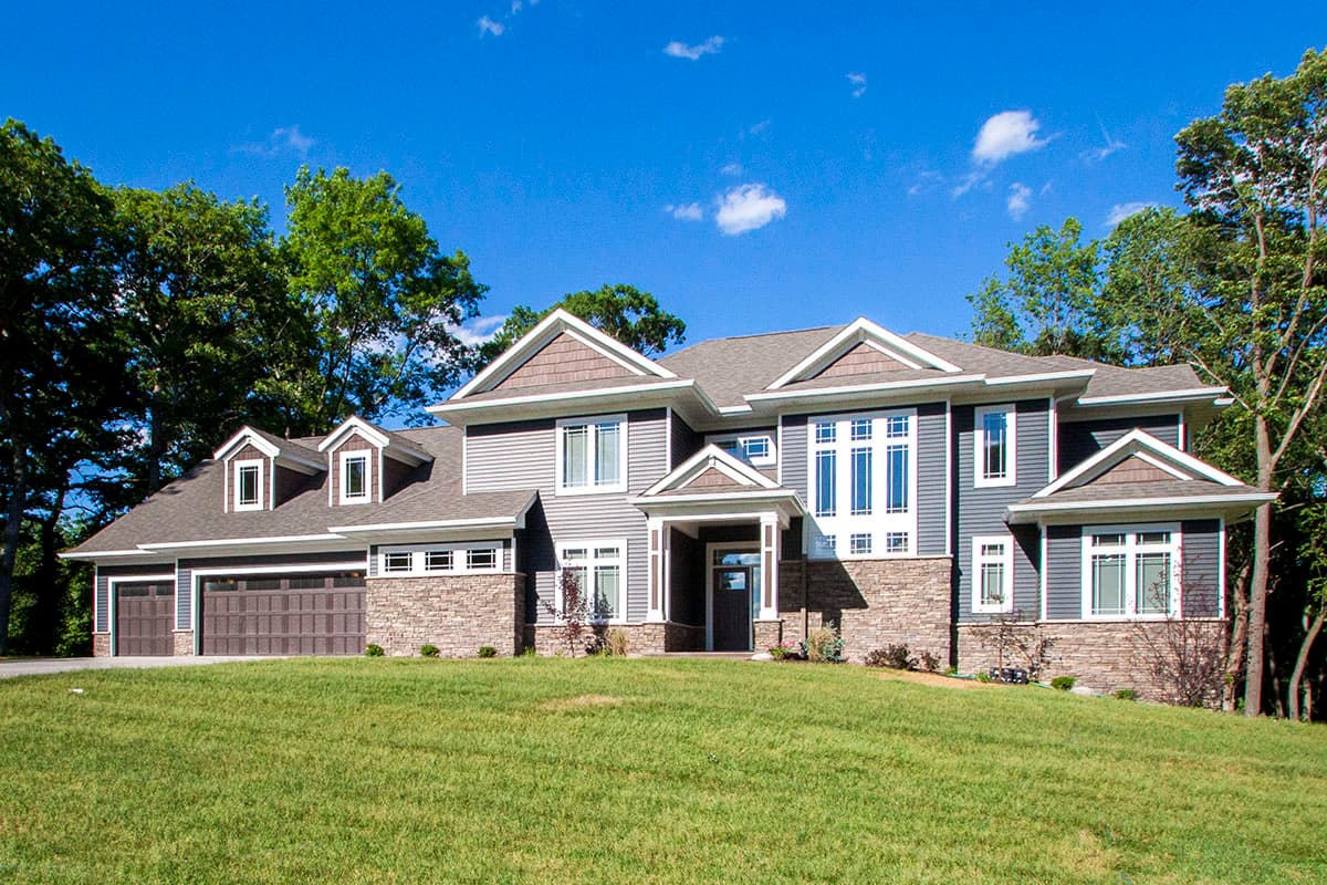 House plan exterior with Craftsman style. Two-story house with dormers, gables, and a prominent front entry porch. Attached garage to the left.