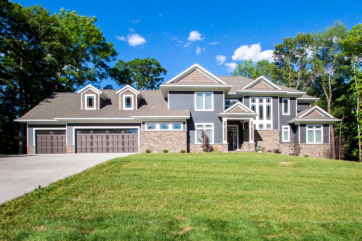 Exterior view of a two-story house plan with a three-car garage, stone accents, dormers, and a covered entry.