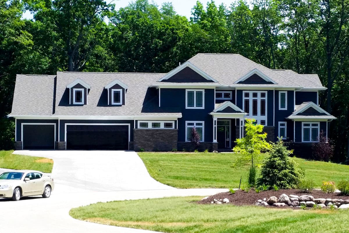 House plan exterior: Two-story dark blue home with three-car garage, gables, dormers, and covered entry.