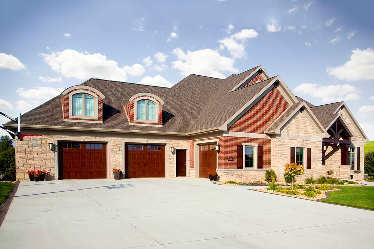 House plan exterior with brick and stone facade, three-car garage, and arched dormer windows.