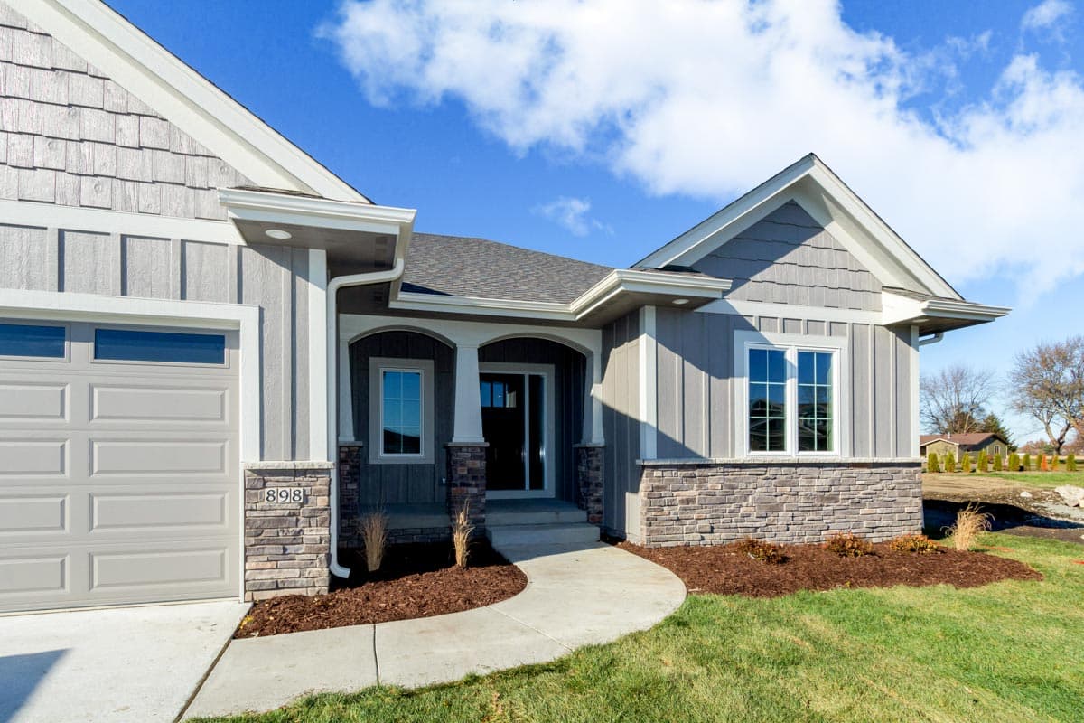 House plan exterior with shingle and board-and-batten siding, stone accents, arched entryway, and attached garage.