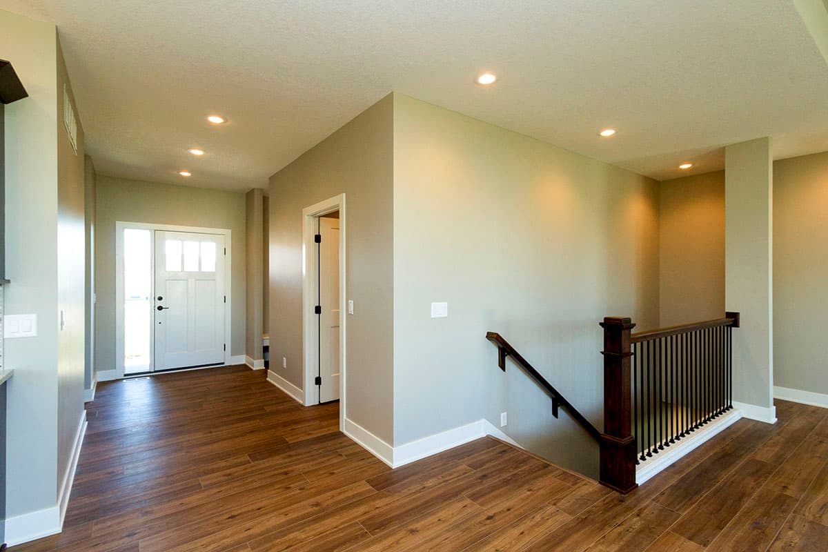 Interior view of a house entry with a white front door, wood flooring, and a staircase with dark wood railing.
