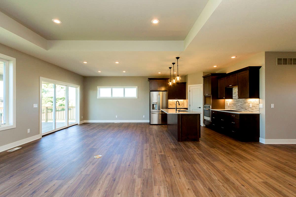 Open concept living area and kitchen with large windows, island, dark cabinets, stainless steel appliances, and coffered ceiling.