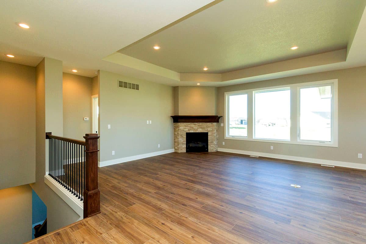 Great room with stone fireplace, tiered ceiling with recessed lighting, and large bay window.