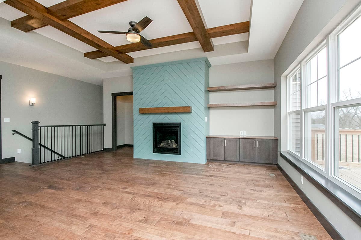 Interior view of a living room with a coffered ceiling, wood beams, fireplace, and large windows.
