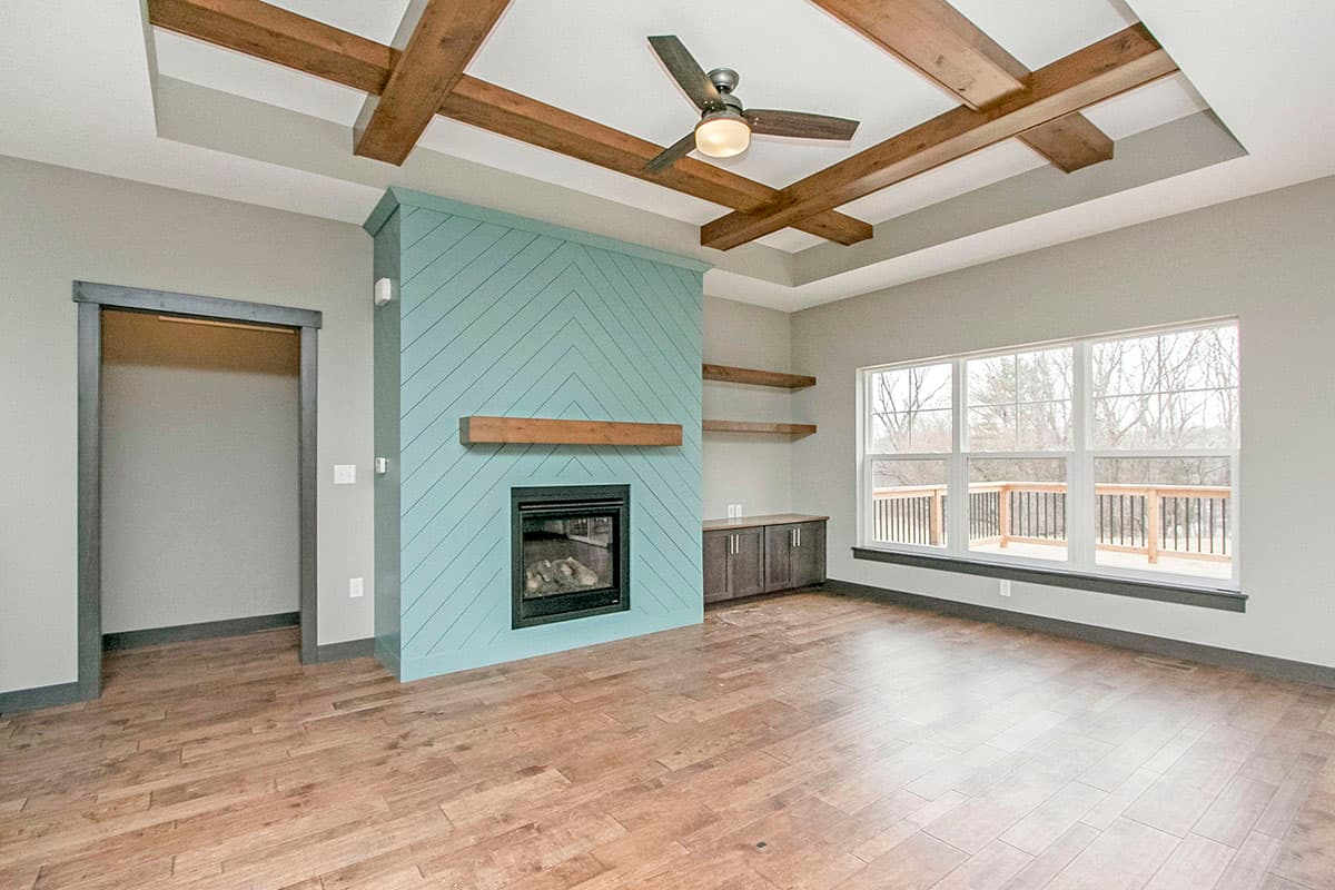 Living room with coffered ceiling, teal fireplace with wood mantel, built-in cabinets, and large windows.