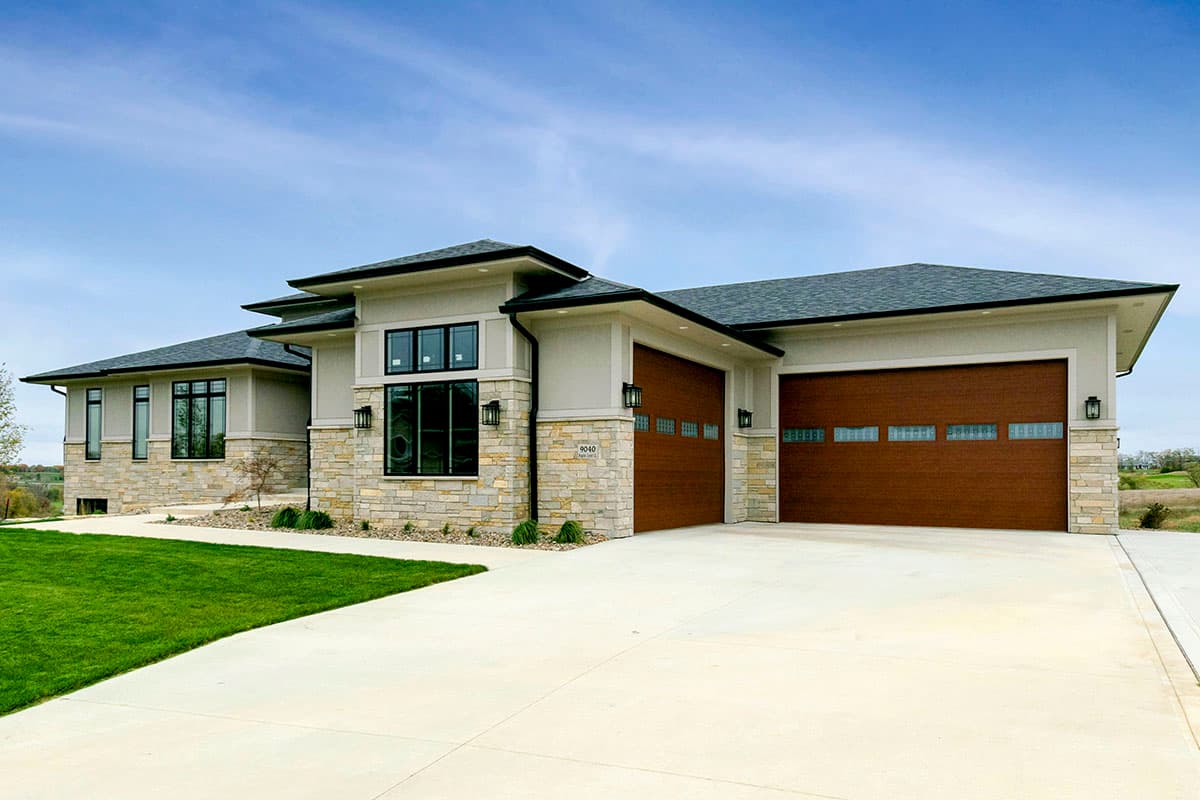 Modern style house plan exterior, one story, featuring stone accents, cantilevered rooflines, large windows, and a three-car garage with wood doors.