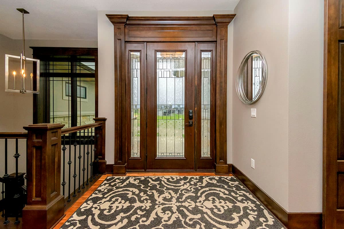 Interior view: Entryway with double doors featuring leaded glass, dark wood trim, a patterned rug, and a modern chandelier.