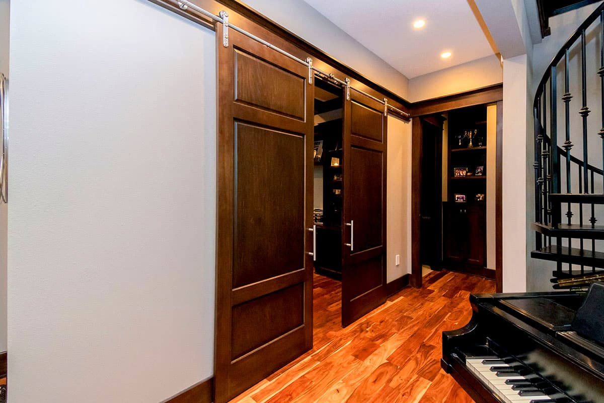 Interior view of two dark wood panel barn doors on metal tracks, opening to a room with built-in shelves.