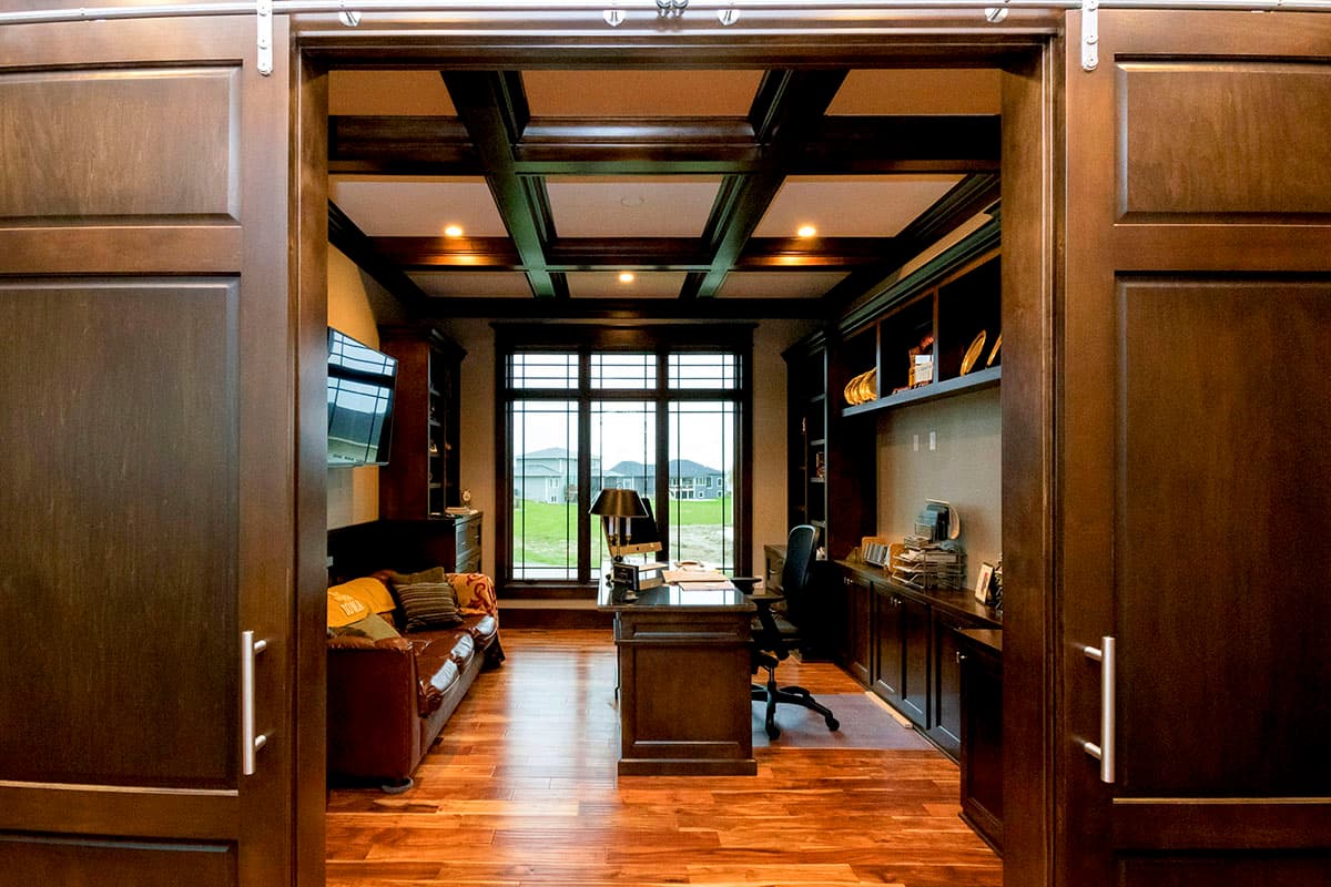 Office interior with coffered ceiling, built-in bookshelves, desk, leather sofa, and large grid windows.