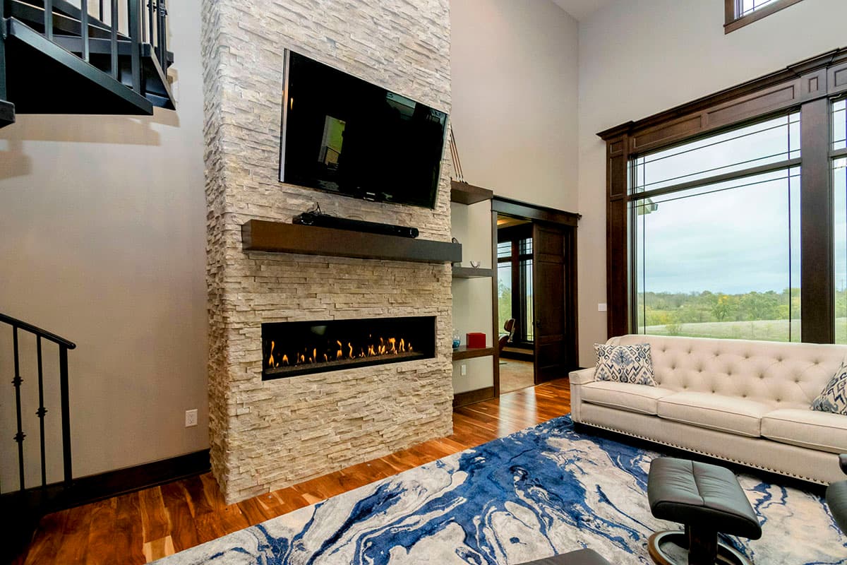 Living room with floor-to-ceiling stacked stone fireplace, linear gas fire, media console, and large windows.