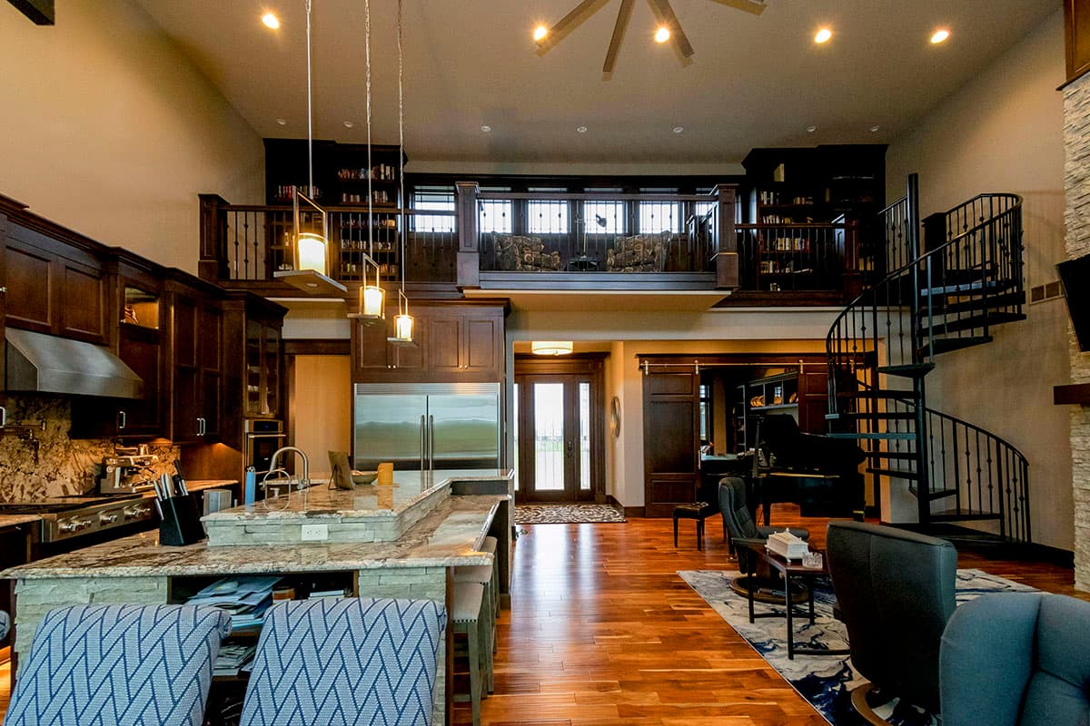 Open concept living area with kitchen, dining, and seating areas, featuring a loft, spiral staircase, and stone fireplace.