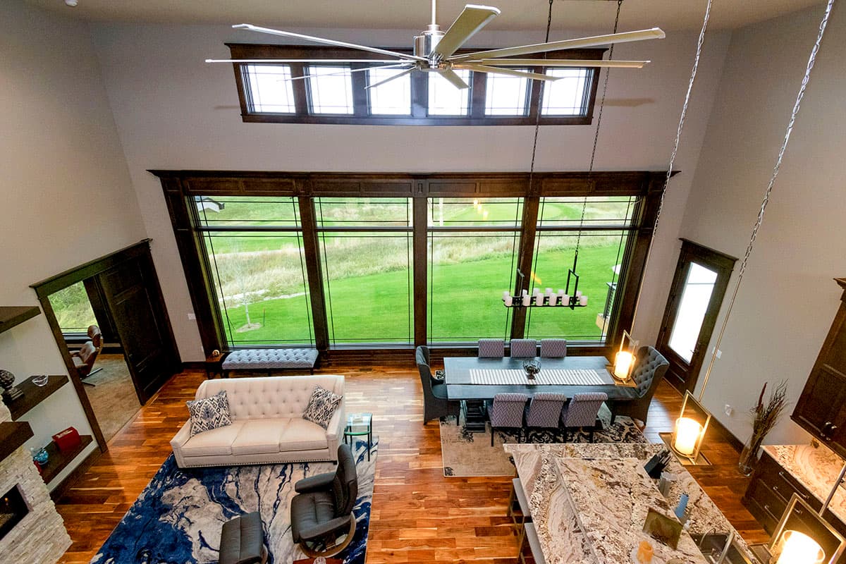 Open concept living and dining area with large windows, a spacious kitchen island, and a vaulted ceiling with a ceiling fan.