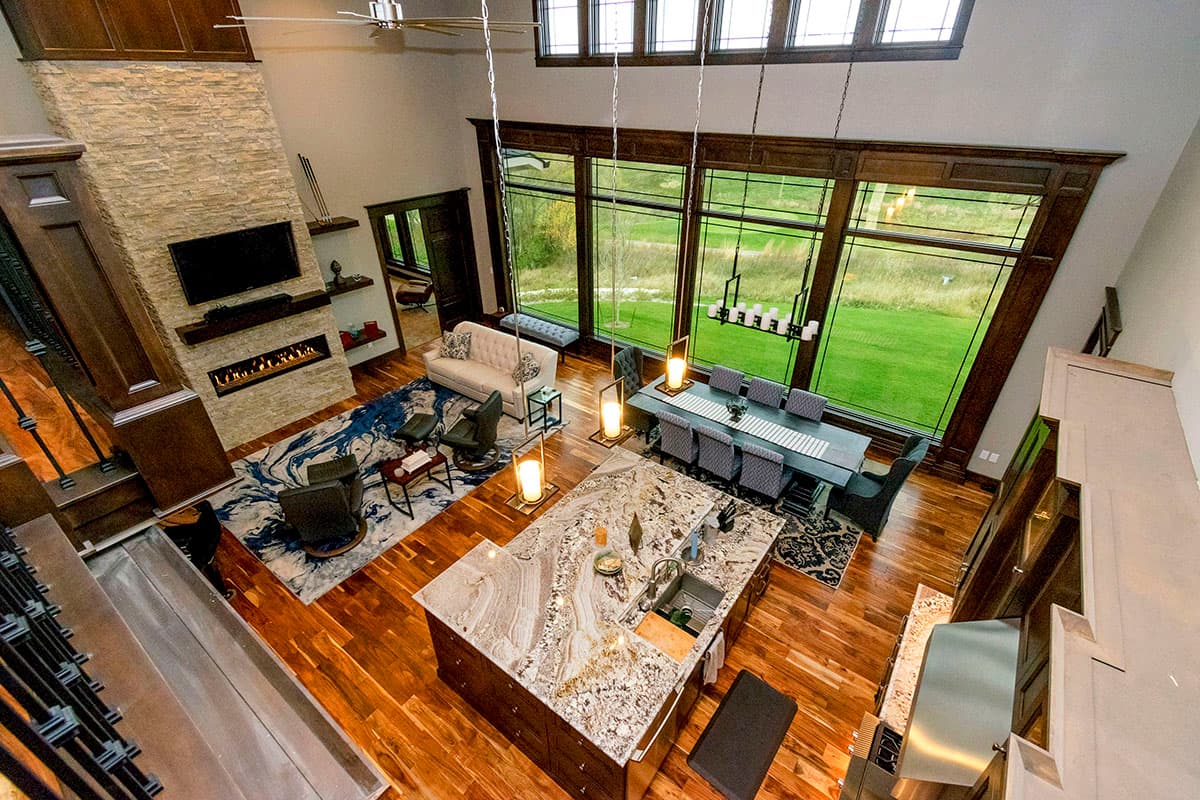 Open-concept great room with stone fireplace, large island kitchen, dining area, and expansive windows.